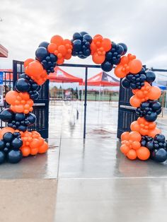 an orange and black balloon arch on the ground