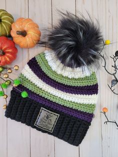 a knitted hat with a black pom - pom sits next to pumpkins