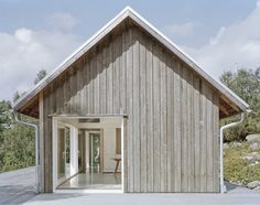 a wooden house sitting on top of a cement floor next to a lush green field