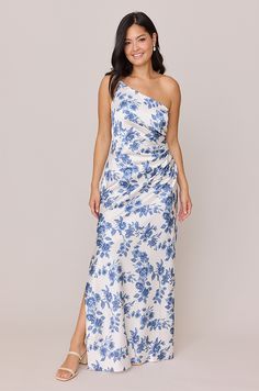 a woman wearing a blue and white floral print one shoulder dress with thigh high slit