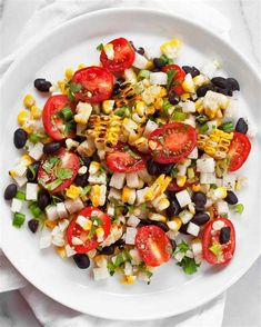 a white plate filled with corn, tomatoes and black beans on top of a table