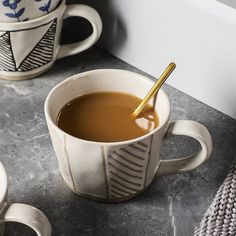 a cup of coffee with a spoon in it on a counter next to two mugs