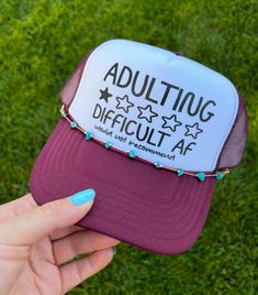 Turn heads with the Otto® 'Adulting Difficult' Foam Snapback Cap w/Chain. This unique hat features a high-quality foam front panel and breathable mesh back for ultimate comfort and style. The playful 'Adulting Difficult' graphic, combined with a trendy chain detail, adds a bold and cheeky twist to your casual look. Perfect for parties, social events, or adding a fun statement to your everyday outfit. The adjustable snapback closure ensures a perfect fit for all-day wear. Elevate your accessory game with this eye-catching and humorous trucker hat. Shop now to add this standout piece to your collection! Specs: * Fabric: 55% Foam, 45% Nylon * Closure: Plastic Snapback * Fit: One Size Fits Most * Panels: 5 * Crown: Mid; Structured * Visor: Curved The Mid Profile 5 Panel Foam Trucker Hat is con Vinyl Hat, Fun Hats, Unique Hats, Everyday Outfit, Cool Hats, Custom Vinyl, Social Events, Snapback Cap, Trucker Cap