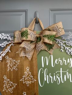 a merry christmas sign hanging on the front door with snowflakes and evergreens