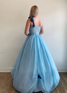 "This is a vintage 1950's light blue tone wedding dress. It is gives strong Cinderella vibes with the color and fit. The dress has a synthetic light blue tone lining, a layer of blue tone tulle, and a soft chiffon-type outer layer in the same light blue tone. The bodice is fitted and has a side zipper. The skirt has small pickups at the hem accentuated by a medium blue tone velvet bow. The dress also has a one shoulder strap finished in a bow in the same medium blue tone velvet. The dress has a Light Blue Ball Gown For Debutante Ball, Light Blue Ball Gown With Fitted Bodice For Wedding, Vintage Blue Dress For Wedding, 1950s Style Blue Wedding Dress, Blue Tone Wedding, Small Pickups, Blue Tone, Vintage Gowns, Wrap Shawl