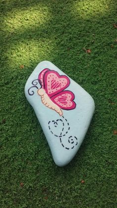 a painted rock sitting in the grass with a butterfly on it's back end