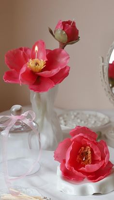 two pink flowers in a white vase on a table next to a mirror and other items