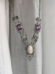 Antique necklace in silver tone metal filigree, mounted with a cameo and two purple glass stones. The stones have beautiful reflections and are in good condition. The necklace is not in excellent condition and shows signs of wear corresponding to its age, but it can still be worn and remains a very beautiful jewel. The metal is oxidized in several places and the chain has a damaged link, which however seems secure if not pulled (see last picture). Length: about 46 cm. Formal Purple Metal Necklace, Silver Cameo Metal Necklace, Silver Metal Cameo Necklace, Vintage Purple Filigree Necklace, Silver Metal Cameo Jewelry, Purple Vintage Filigree Necklace, Ornate Silver Amethyst Necklace, Victorian Cameo Silver Necklace, Cameo Necklace