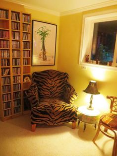 a zebra print chair sitting in front of a book shelf filled with books next to a lamp