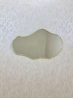 an oval mirror on the wall above a sink in a bathroom with white walls and gold trim