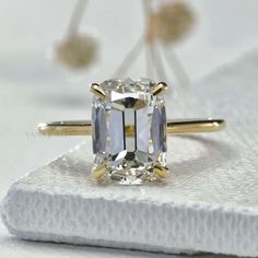 an emerald cut diamond sits on top of a white napkin with two gold rings around it