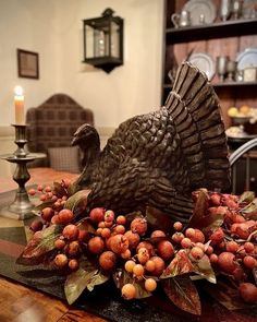 a turkey statue sitting on top of a wooden table next to berries and candle holders