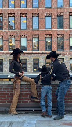 two men and a woman standing next to each other near a brick wall in front of a building