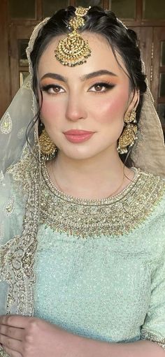 a woman wearing a bridal veil and headpiece with gold jewelry on her face