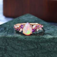 an opal and diamond ring sits on a green surface