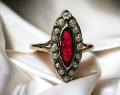 a close up of a ring with pearls and a red stone in the center on a white cloth