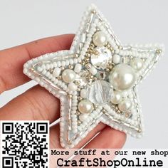 a hand holding a white beaded star brooch with pearls and beads on it