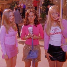 three young women standing next to each other talking on their cell phones and holding purses