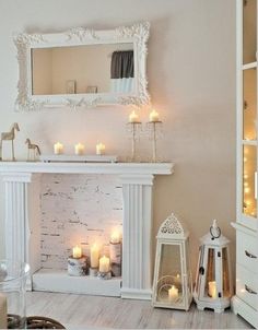 a living room filled with lots of white furniture and candles in front of a fireplace