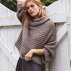 a woman leaning against a fence wearing a sweater