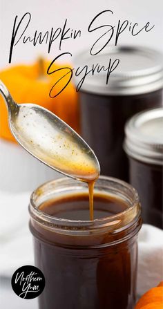 a spoon full of pumpkin spice syrup being poured into a jar with an orange in the background