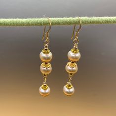 Unique presentation of peach freshwater pearls, antique gold spacers, and filigree bead caps in these elegant dangle earrings. The dangles are connected to each other and to the gold filled earwire through gold filled wrapped loops.  The earrings are about 1 1/4 inches long, measured from the earwire, and come nestled comfortably on a bed of cotton in a white cardboard box. Made in the USA by me. NA-821-0624-1111 Gold Pearl Drop Beaded Earrings, Gold Beaded Earrings With Pearl Drop For Gifts, Gold Beaded Pearl Earrings, Gold Pearl Drop Beaded Earrings For Gift, Gold Pearl Earrings With Gold Beads, Delicate Gold Earrings With Dangling Beads, Elegant Gold Pearl Earrings With Gold Beads, Pearl Drop Earrings With Gold Beads, Handmade Gold Pearl Beaded Earrings