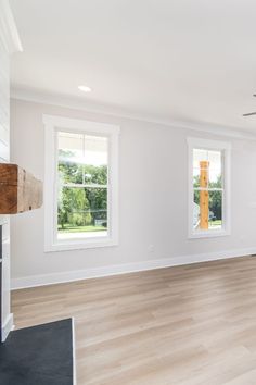 an empty living room with white walls and wood flooring in the foreground is a ceiling fan