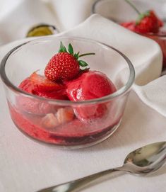 strawberries in a glass bowl on a white tablecloth with spoons and napkins