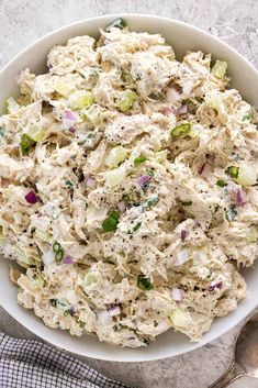 a white bowl filled with chicken salad on top of a table next to a fork