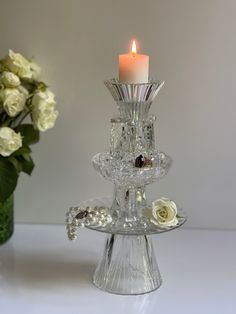 a candle that is sitting on top of a glass stand with flowers in the background