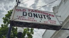 an old fashioned donut shop sign hanging off the side of a building in front of a tree