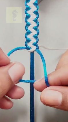 two hands are working on an object with blue and white yarn in the shape of a heart