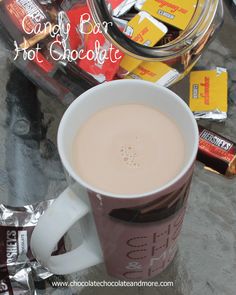 a cup of hot chocolate sitting next to some candy bar's on a table