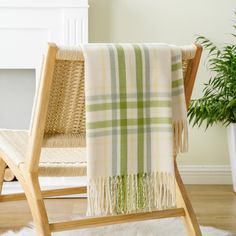 a green and white plaid blanket on a wooden chair next to a potted plant