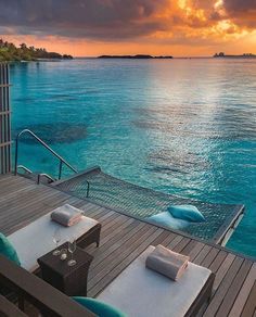 an outdoor dining area with tables and chairs on the deck overlooking the ocean at sunset