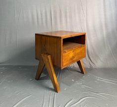 a small wooden table with two legs and a drawer on one side, against a white backdrop