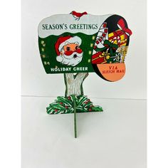 a green and white christmas card holder with santa claus on it's head, holding a sign that says season's greetings holiday cheer