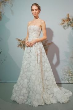 a woman standing in front of a wall wearing a white dress with flowers on it