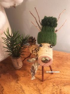 a wooden table topped with two plants and a wine cork head decoration on top of it