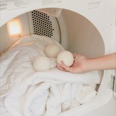 a person holding three eggs in front of an open washing machine with white sheets on it