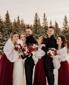 a group of people standing next to each other in front of snow covered trees and holding bouquets