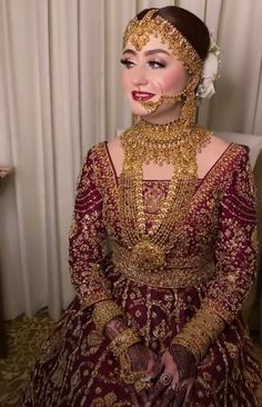 a woman in a red and gold wedding dress with jewelry on her face, sitting down