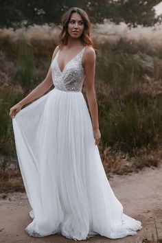 a woman in a white dress standing on a dirt path with her arms behind her back