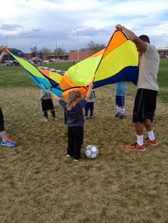 a group of people standing on top of a grass covered field holding onto a kite