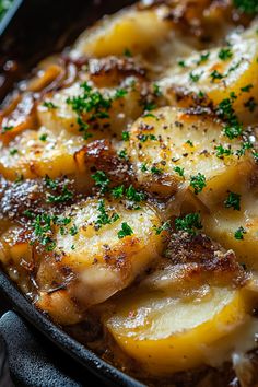 a pan filled with potatoes and meat covered in parmesan cheese, garnished with green herbs