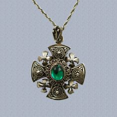 "This ornate Jerusalem Cross pendant is composed of pure silver and features a green cabochon at the center. The pendant has a layered construction with a solid platform topped by convex decorative elements. The surface of the pendant is highly detailed with extensive granulation and wire work and has 4 crosses with brightly polished surfaces at each corner. The pendant comes with its original fan-shaped bail which also bears ornamental granulation and wirework. The back of the bail is fitted wi Ornate Cabochon Round Pendant Jewelry, Ornate Round Pendant Cabochon Jewelry, Ornate Round Cabochon Pendant Jewelry, Traditional Oval Cabochon Necklace, Traditional Oval Cabochon Necklaces, Green Byzantine Style Round Jewelry, Handmade Green Byzantine Jewelry, Green Oval Pendant Necklace With Engraving, Green Oval Pendant Necklace Engraved