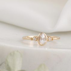 a white diamond ring sitting on top of a white cloth covered table next to a plant