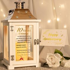 a white rose sitting next to an old fashioned clock and anniversary card holder with happy anniversary written on it