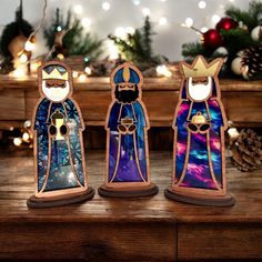 three stained glass nativity figurines sitting on a table with christmas lights in the background