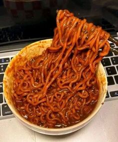 a bowl filled with noodles sitting on top of a laptop computer next to a keyboard